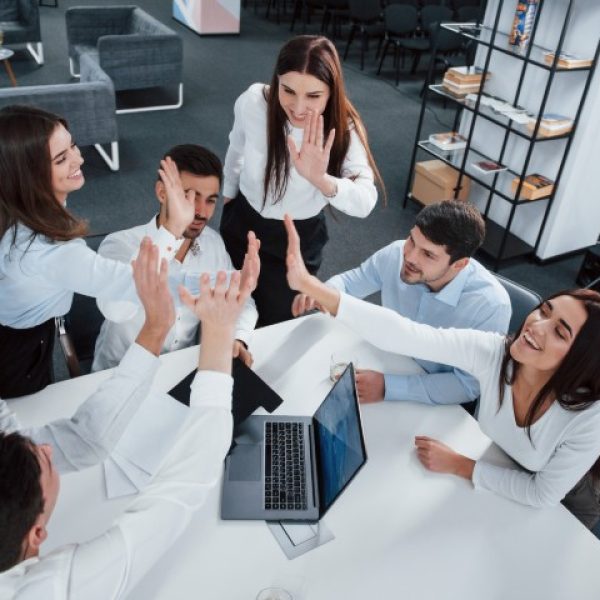 Giving high five to each other. Top view of office workers in classic wear sitting near the table using laptop and documents.