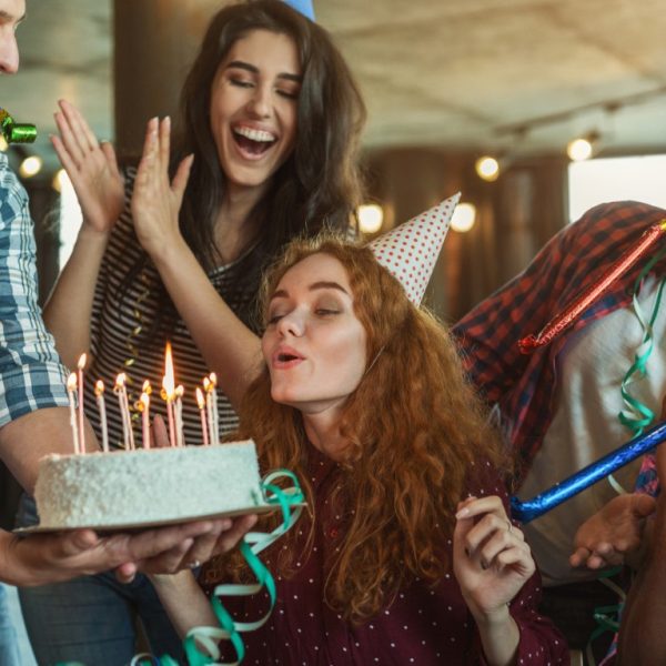 Happy birthday girl is blowing candles on holiday cake and making wish, copy space
